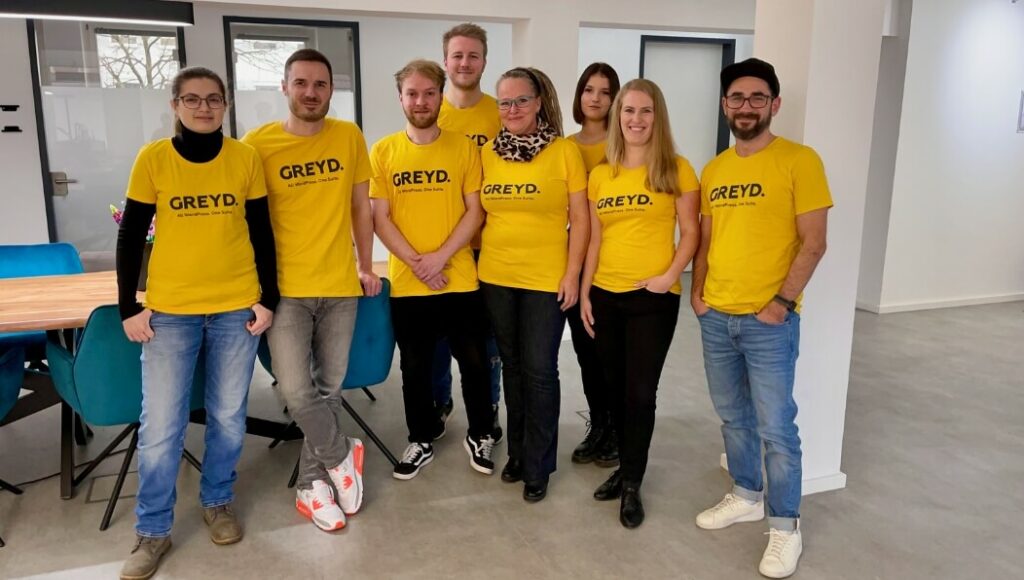 Greyd Team photo. Four women and four men, all wearing a yellow T-shirt with the Greyd text logo.