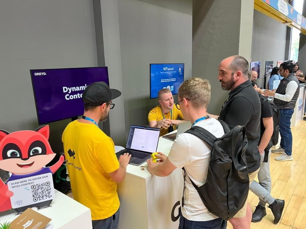 A group of people seen form behind, visiting the booth of Greyd.