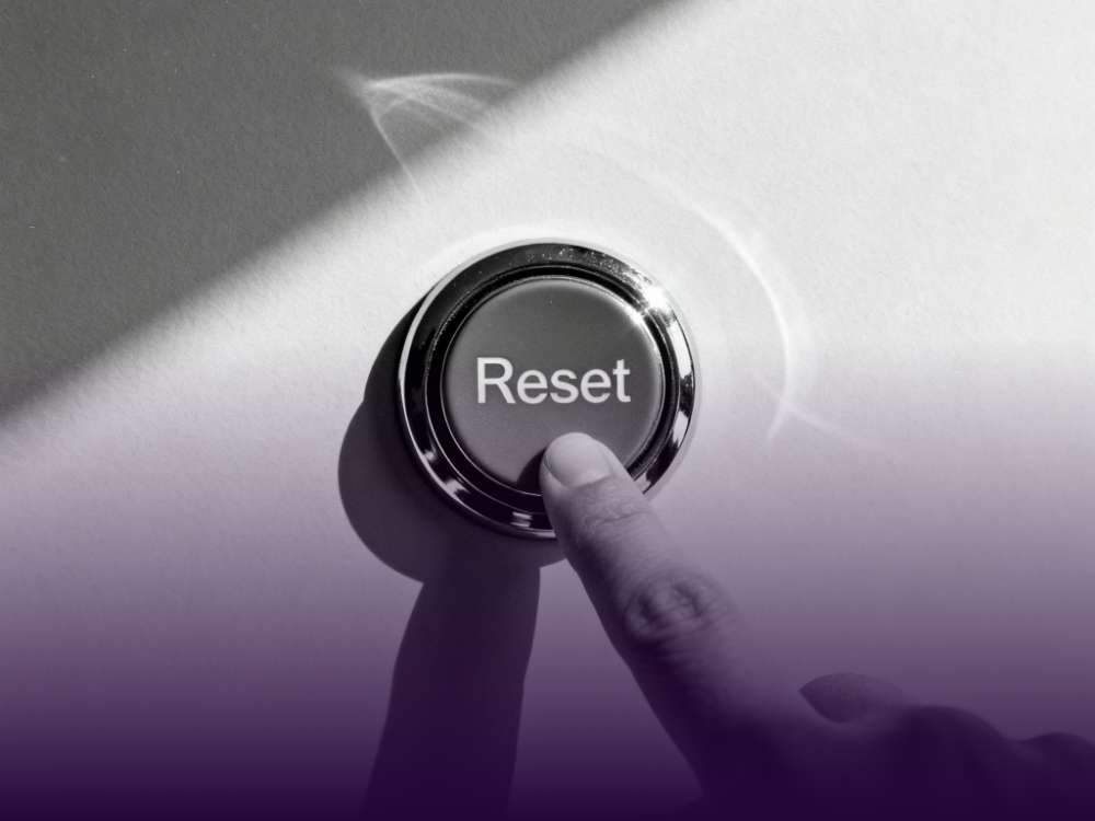 Finger drückt einen Knopf mit dem Titel "Reset", schwarz weiß und lila Farben.